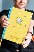The yellow and turquoise Positive Doodle Diary being held towards the camera 