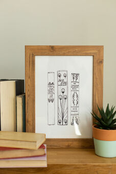 A framed print of a black and white illustration of three book spines by Georgina The Librarian