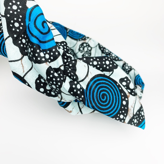 A black woman gazing downwards, wearing a blue African fabric print wire headband