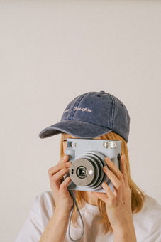 Girl in embroidered cap that says Happy thoughts taking picture with polaroid camera