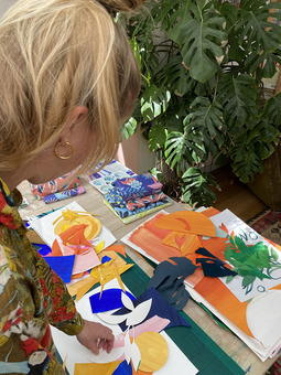 Image of Charlotte working on a collage on her desk with lots of colourful pieces of paper.