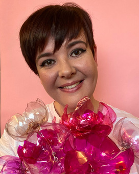 Aimee smiling against a pink background holding a big bunch of hot pink recycled plastic bottle flowers
