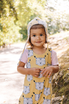 Child girl wearing yellow snow leopard romper and winter hat outdoors smiling face on.