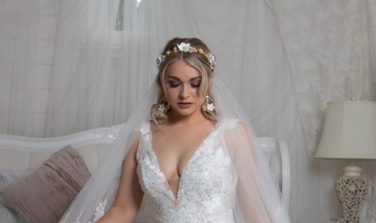 A bride sits on the end of a bed in her wedding dress and accessories