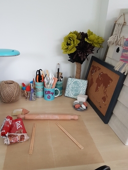 A picture showing a desk in Seema's work area. It has a pack of open clay, a rolling pin and cups of various tools.