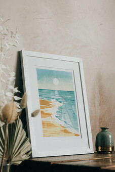 Framed print of a beach seascape at sunrise leaning against a wall.