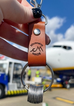 Female holding a tan Journeys Made leather travel keyring with stainless steel tokens on it, black painted nails, and a Ryanair airplane in the background