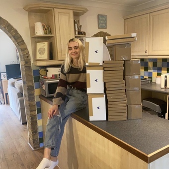 Girl sat on counter smiling holder a pile of postal boxes