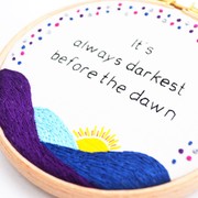 a hand embroidered sunrise with the text 'It's always darkest before the dawn'