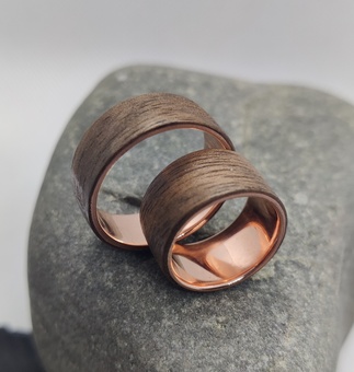 Two copper rings wrapped with european walnut wood, both resting on a rock. 