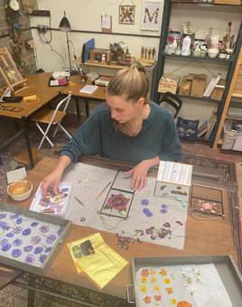 Elsker Creations studio with Sian working at her desk on a botanical artwork using pressed flowers and gold leaf