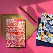 A pile of patterned A5 hardcover OlaOla notebooks with assoicated artwork and a silk stain headband.