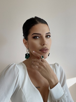 Woman in white shirt wearing green earrings and ring 