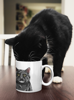 A tuxedo cat drinking out of a mug with their pet portrait on