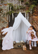 Girl enjoying a tea party under a white vintage canopy with the tea on a vintage suitcase and a pink floral bunny cut out