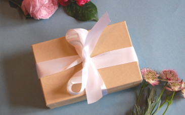 an image of a gift box tied with white ribbon next to some flowers