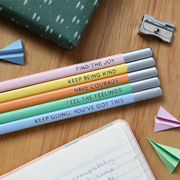 Five pastel pencils with positive phrases on lay on a wooden desk.