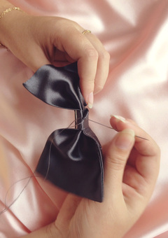 close up of hand sewn finishing a dark grey silk hair bow