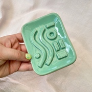 Mint green soap dish being held in my hand up to the camera.