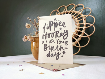 A photo of a card which reads 'today is all about you!' in bold asymmetric hand lettering. in the background is a small plant and a mid century modern mirror.