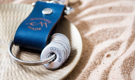 Ocean Blue Leather Travel Keychain with Morocco Engraved Token on a patterned plate laying on sand