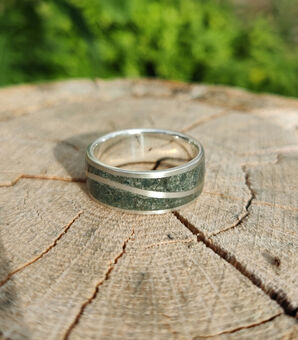 Silver ring with a silver wave, inlaid with green westmorland slate. Sat on a cracked wooden surface with green background