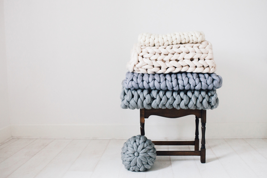 Rose & Wül knitted blankets stacked on a table with a cushion propped against the side
