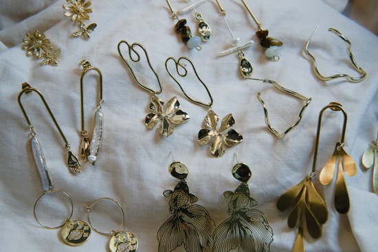 Flat lay of a collection of gold earring designs on a white linen sheet.