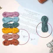 a flatlay of a macrame craft kit showing a rainbow of yarn, copper hoops and instructions