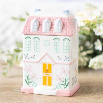 Pastel house-shaped ceramic oil burner and wax warmer featuring a charming design with a pink roof, yellow door, and floral details, placed on a wooden surface 