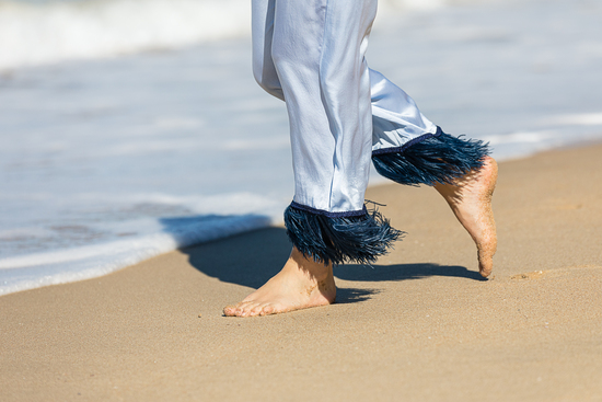 walking person wearing Blue silk trousers with feathers background is a beach with waves