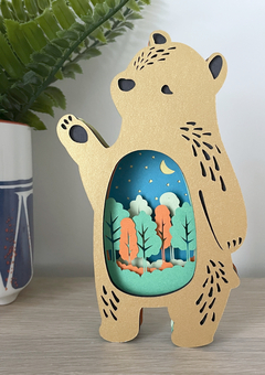 "Forest Friends" bear papercut in gold as a shelf ornament. Cut out section features a moonlit forest scene.