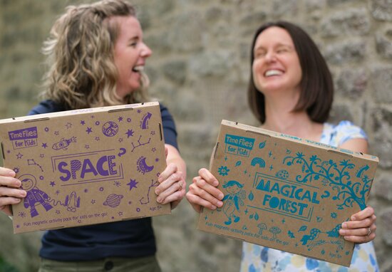 Jill and Lucy (the co-founders of Time Flies for Kids) are laughing and holding up the Space Magnetic Pack and Magical Forest Magnetic Pack.