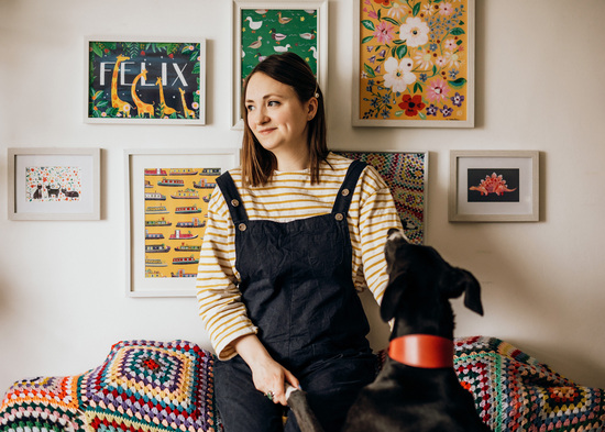 Katie Whitton sitting on a crochet blanket surrounded by prints and Buster the dog.