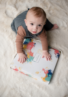 A baby sitting on the carpet with his hands on our baby record book