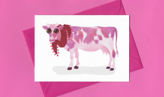 A stylised watercolour illustration on a greeting card of a pink and white cow, wearing sunglasses and a red scarf, with a bright pink envelope on a pink backgr