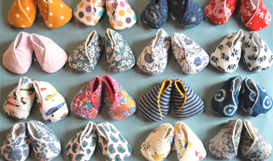 A photo of many pairs of baby shoes in a variety of colours and patterns on a pale blue-grey background