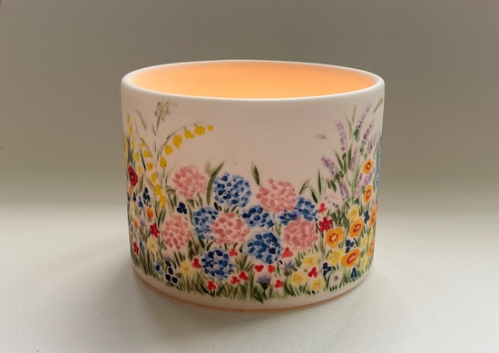 A hand painted tealight holder decorated with a garden flower border design.