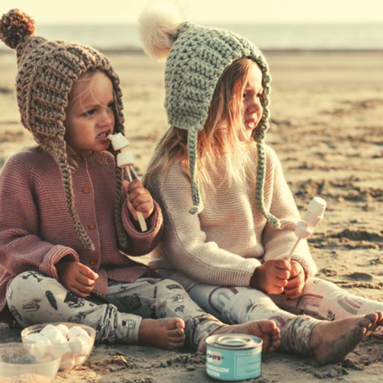 Photo of 2 young girls enjoying toasting marshmallows on the Beach in wooly hats and jumpers