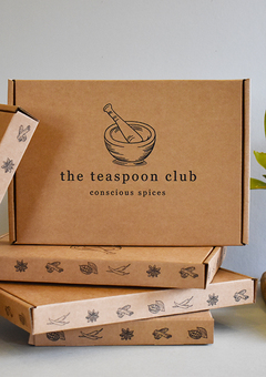 A printed box sits atop 3 stacked boxes. The stacked boxes show illustrated spices along the trim, with a pessle and mortar Teaspoon Club logo on the front