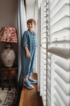 Little boy standing by a window wearing Pip and Henry Sneakers