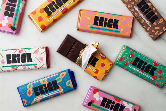 Lots of colourful chocolate bars strewn across a table from above, one is half open to reveal chocolate
