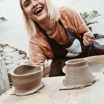 happy pottery class participant making a pot on the potter's wheel
