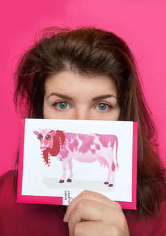 A portrait of our artist Laura, holding a greeting card featuring a stylised watercolour of a pink cow