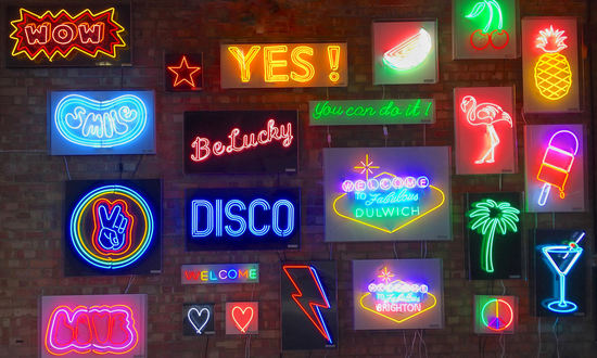 Peckham railway arch with neon signs on brick wall. Disco, rainbow, lollypop, buddah, diamond, CND, peace, anchor love heart