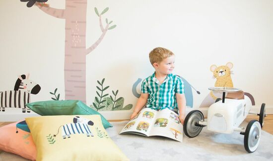 Child sitting reading a book with jungle animal wall decals displayed on the wall with scattered cushions on the floor