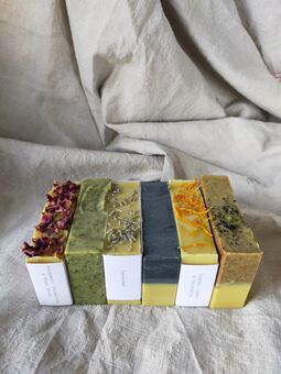 Six different coloured soaps sit together on a oatmeal linen cloth