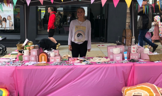 Pictured is a bright pink stall, displaying a variety of products. Behind the table is the owner of Elle&Co, Ellie, smiling happily