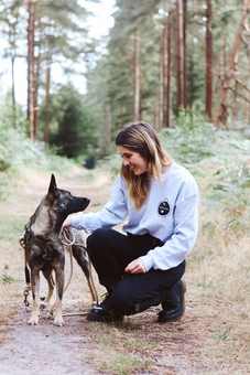 a woman wearing a grey sweater in the woods with her dog
