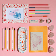 Colourful terrazzo stationery with notebooks and pencils against a pink background